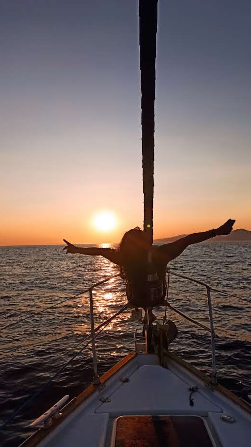 Person seated at the very front of a yacht enjoying the sea breeze in the sunset